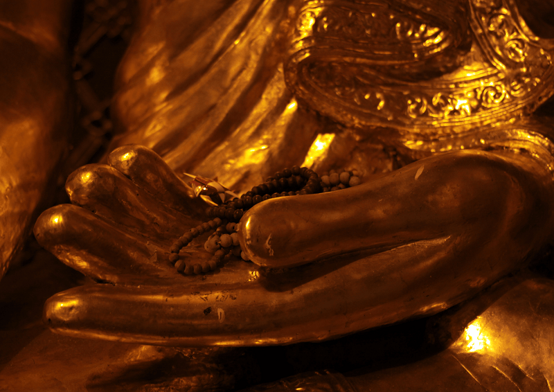 golden buddha hand with prayer beads resting on palm, divine trust by amyra mah
